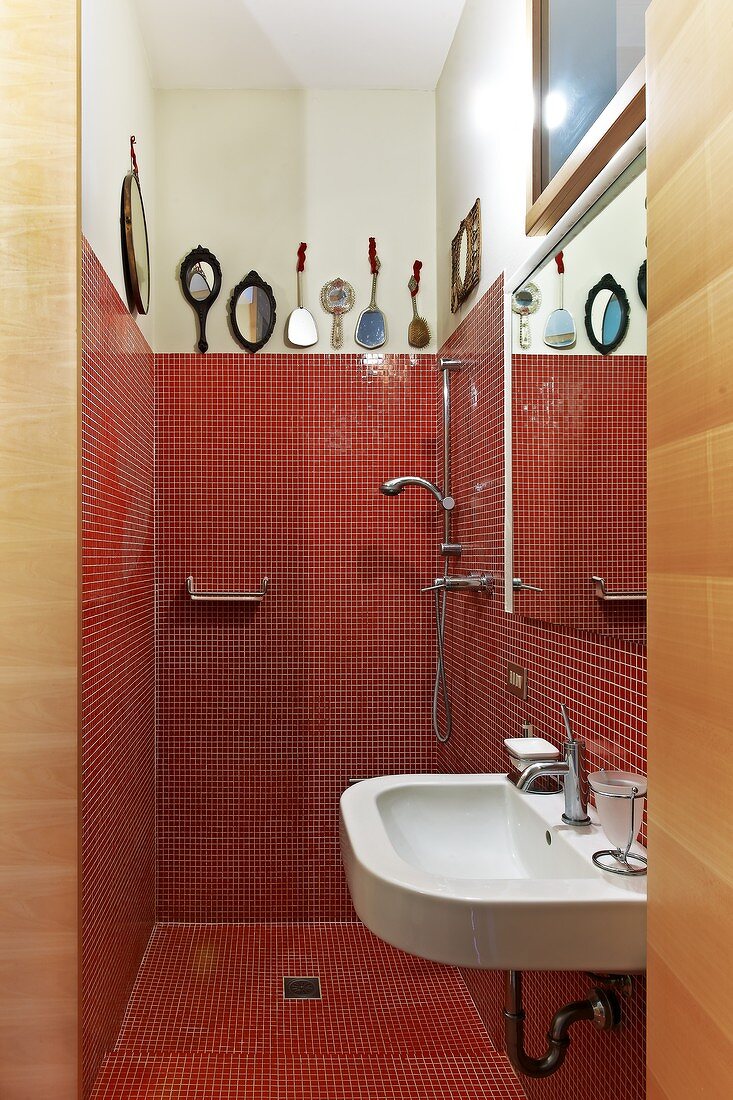 View into bathroom - red mosaic tiles in shower area and plain sink below mirror