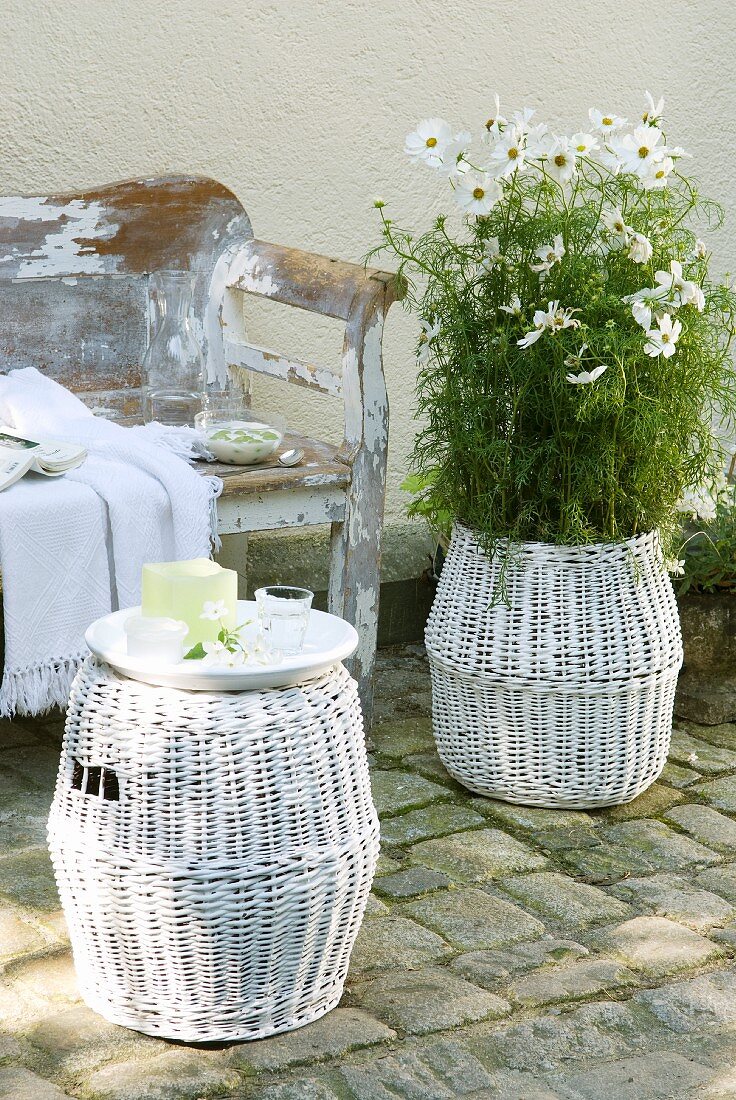 Rattanhocker und passender Übertopf mit weißem Blütenstrauch vor Vintagebank im Shabby Chic