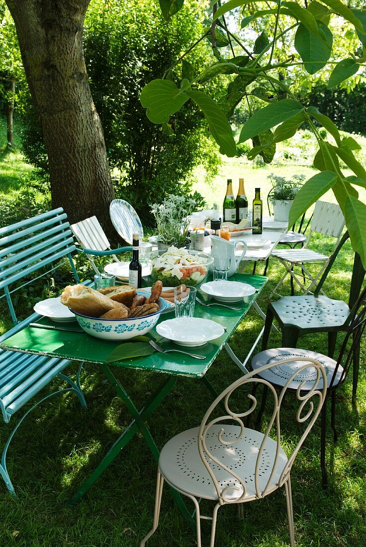 Set table and motley collection of chairs beneath tree for idyllic meal in garden