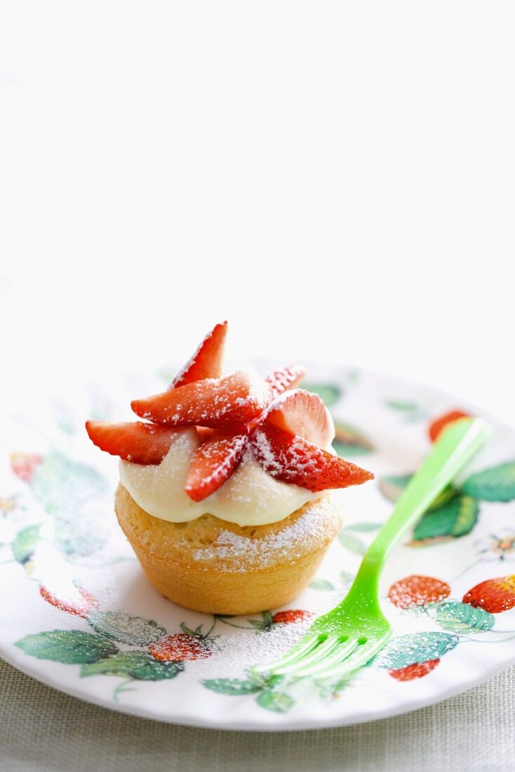 A cupcake topped with white chocolate cream and strawberries