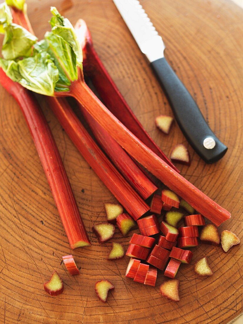 Rhubarb, partially sliced, with a knife on a chopping board