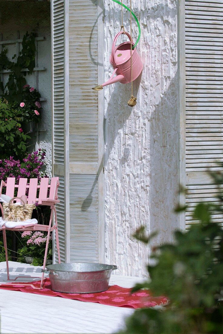 Improvised garden shower on facade of house made from romantic metal watering can, zinc tub and with window shutters as screen