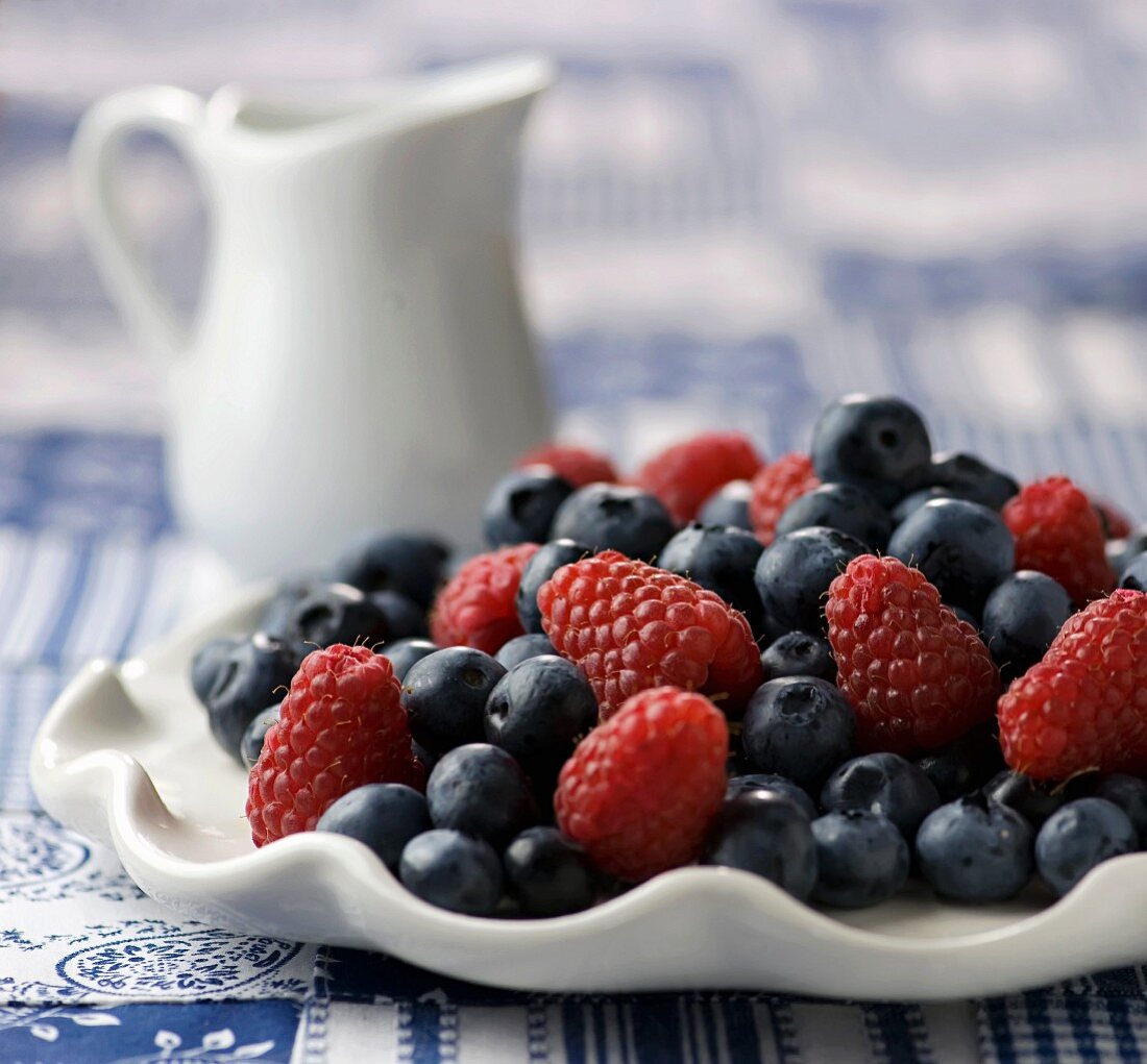Fresh Blueberries and Raspberries on a White Dish; Pitcher