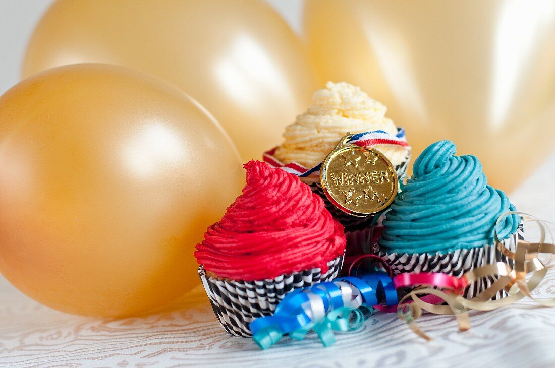 Cupcakes and a medal in front of golden balloons (England)