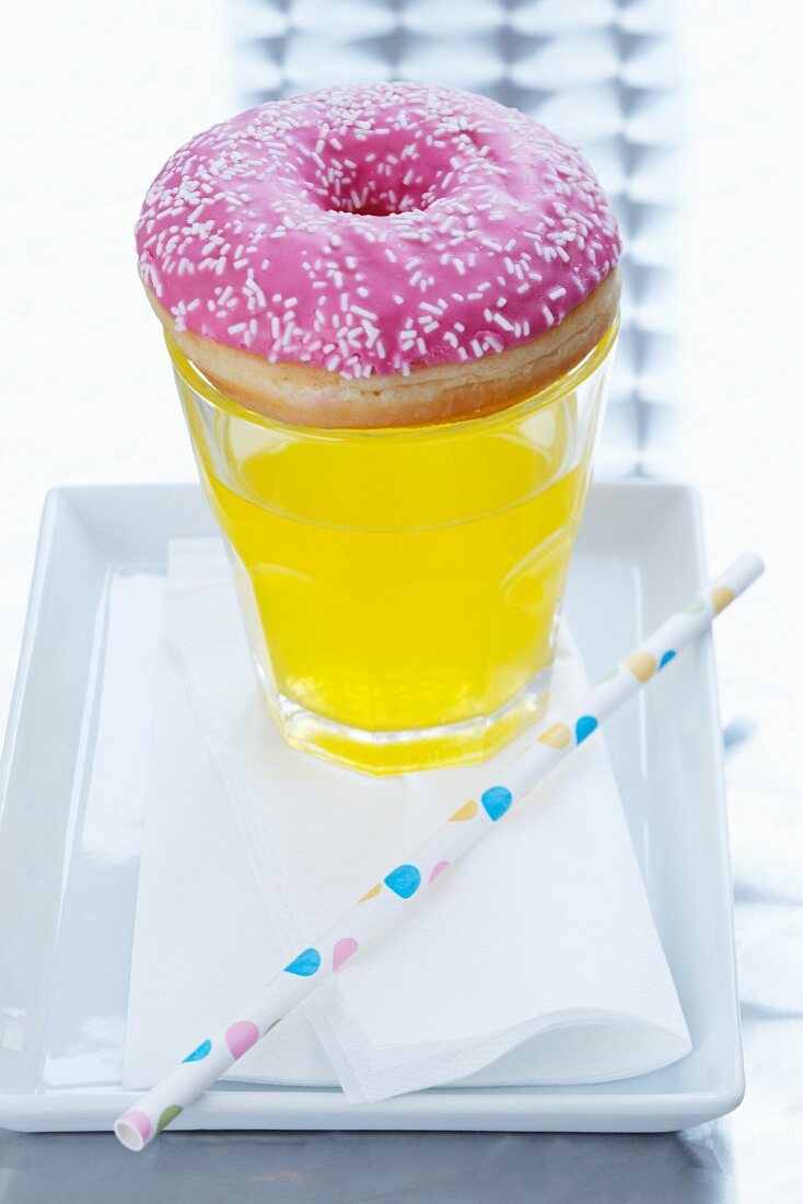 A doughnut on top of a glass of fizzy pop