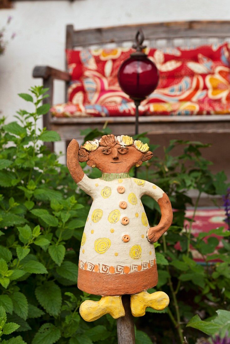 Ceramic figurine in garden with wooden bench on veranda in background