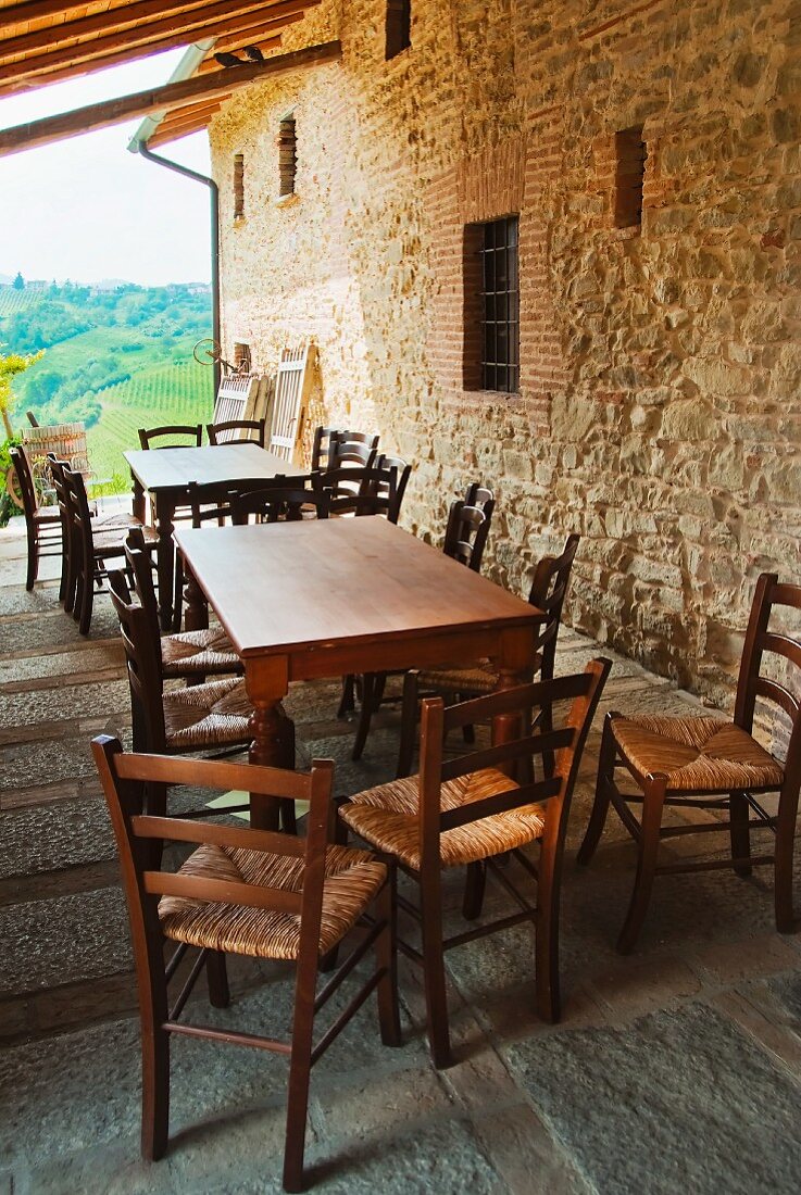 Überdachte Terrasse mit Esstischen und Stühlen neben Natursteinmauer