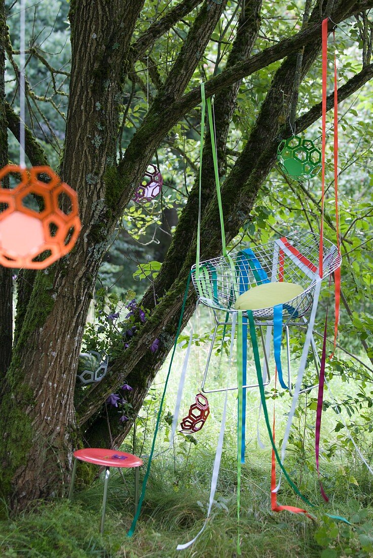 Wire chair hung from tree with colourful ribbons