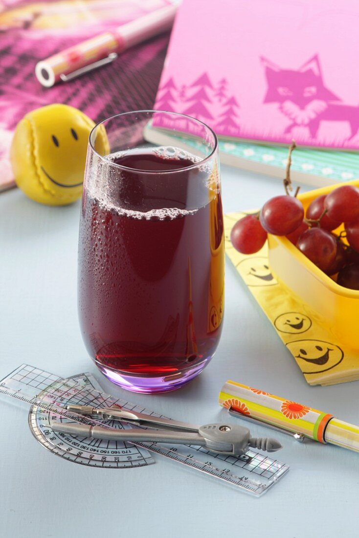 Ein Glas roter Traubensaft zwischen Schulsachen