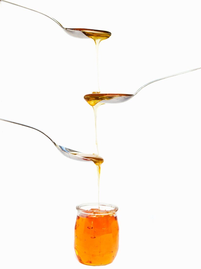 Honey dripping from spoons into a jar