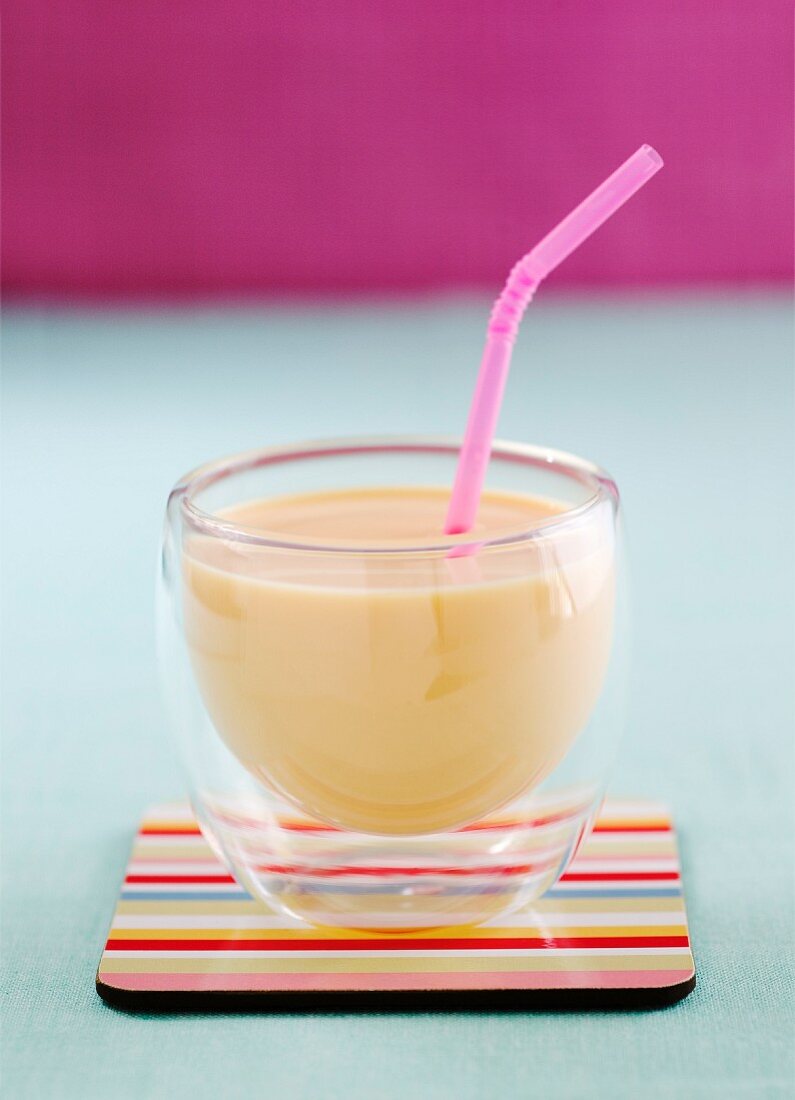 A mango lassi in a glass with a straw