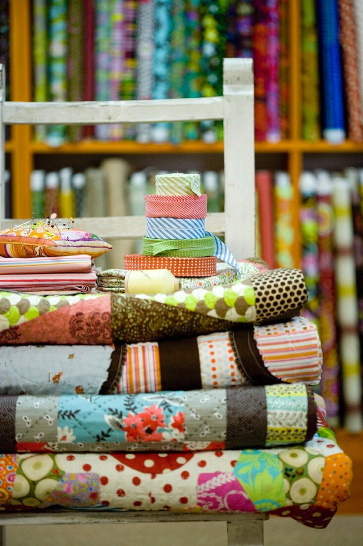 Rolls of patterned fabric on chair in front of shelves of various fabrics