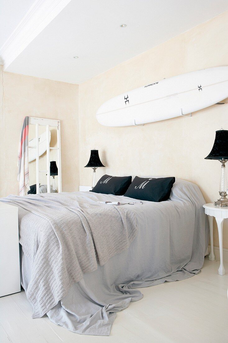 Double bed with grey bed linen and surfboard on wall in bedroom