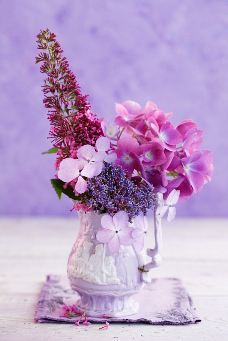 Pinkfarbene Hortensienblüten und Sommerflieder in einer Porzellanvase