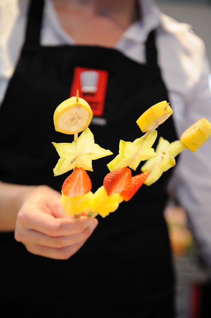 A woman holding three fruit kebabs