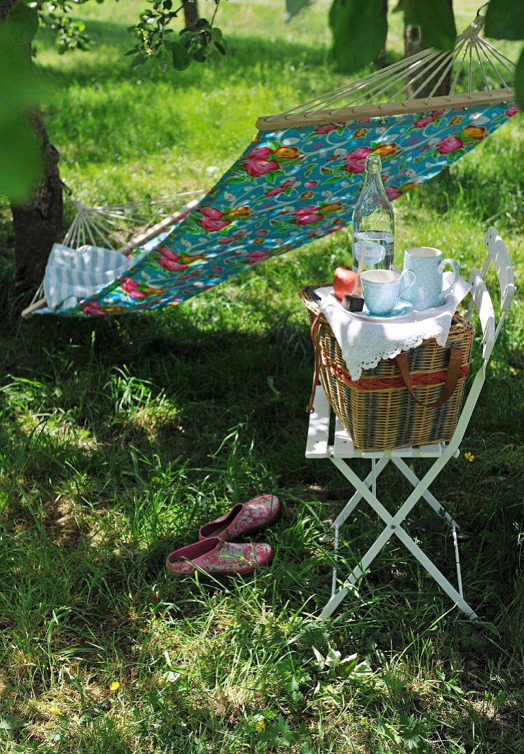 Picnic basket on chair and hammock hung between two trees