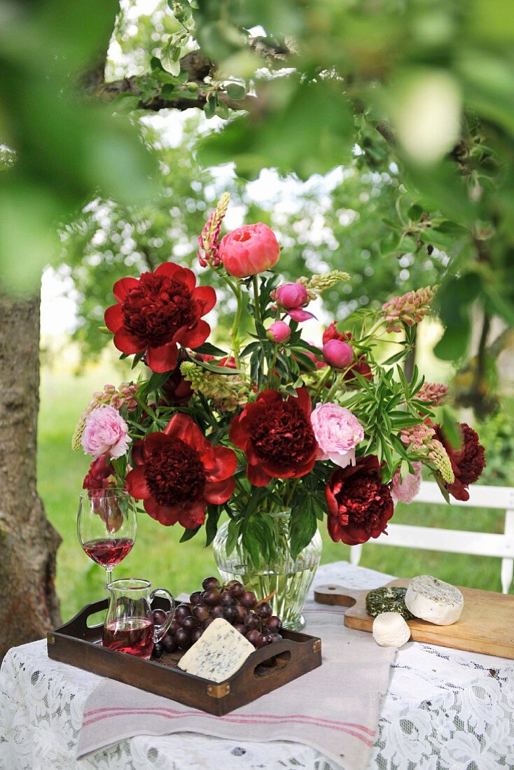 Farbenprächtiger Sommerstrauss mit Tablett und Weinkaraffe auf Gartentisch