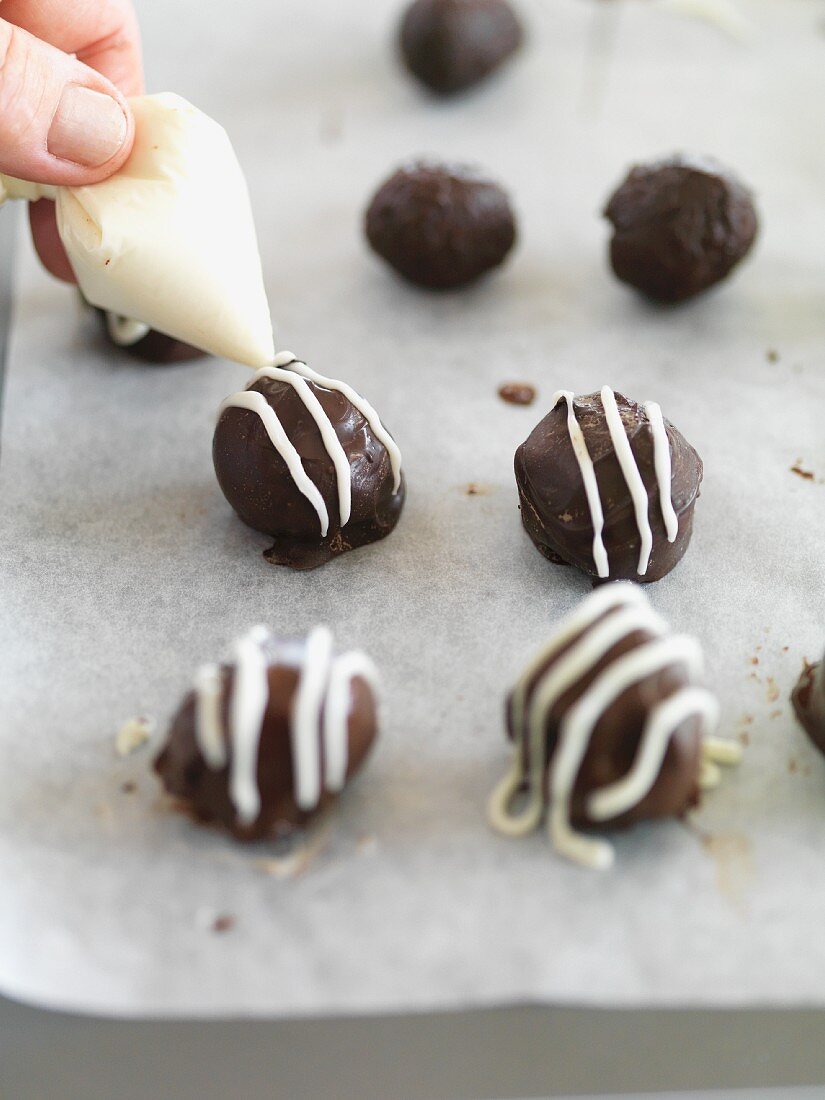 Chocolate pralines being decorated with white chocolate stripes