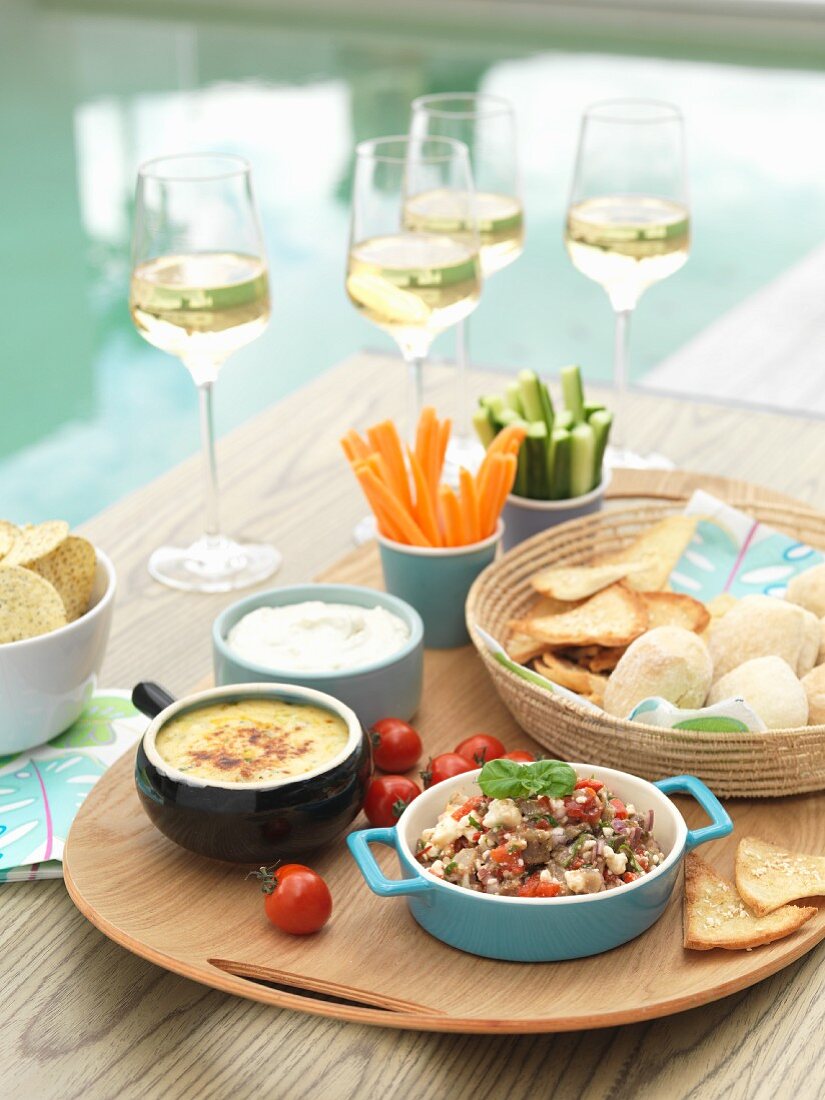 Dips, bread, vegetable crudités and wine by a swimming pool