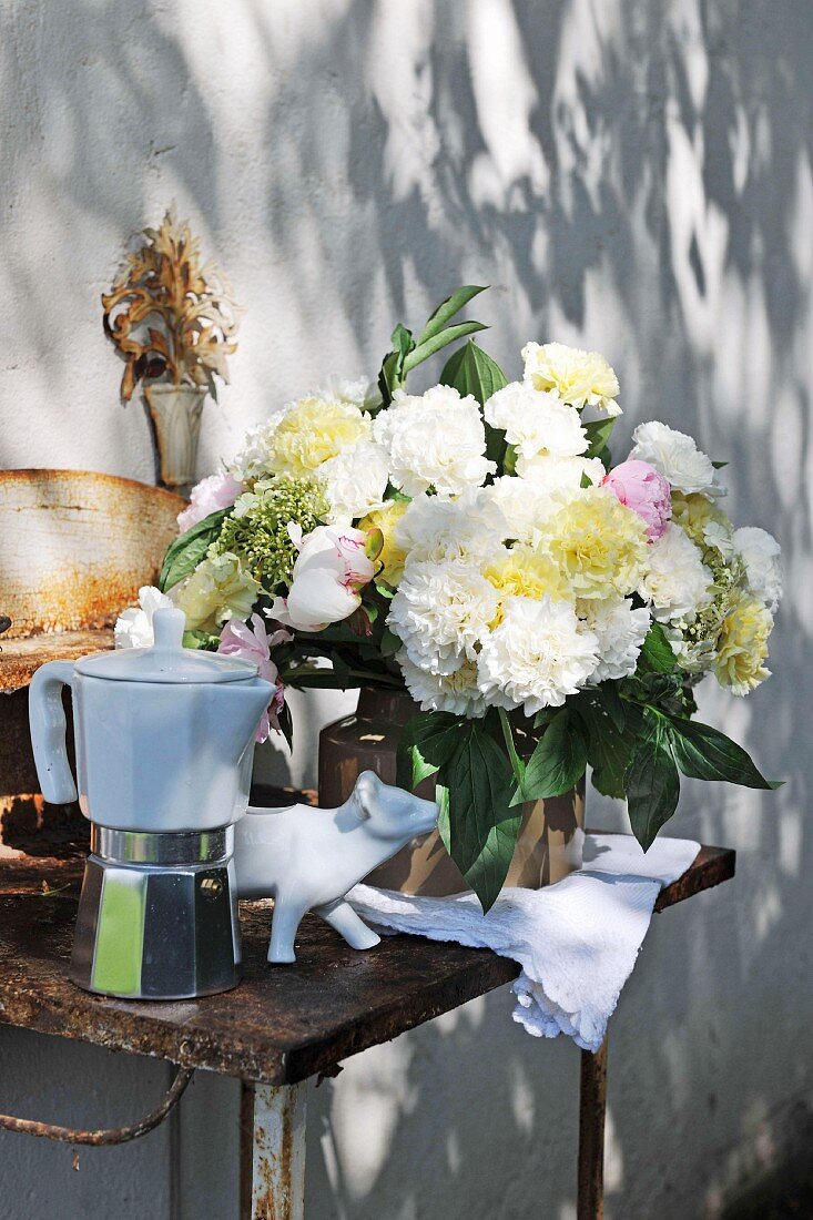 Bouquet of garden flowers and espresso pot on rusty table with patterns of shadows and light on wall