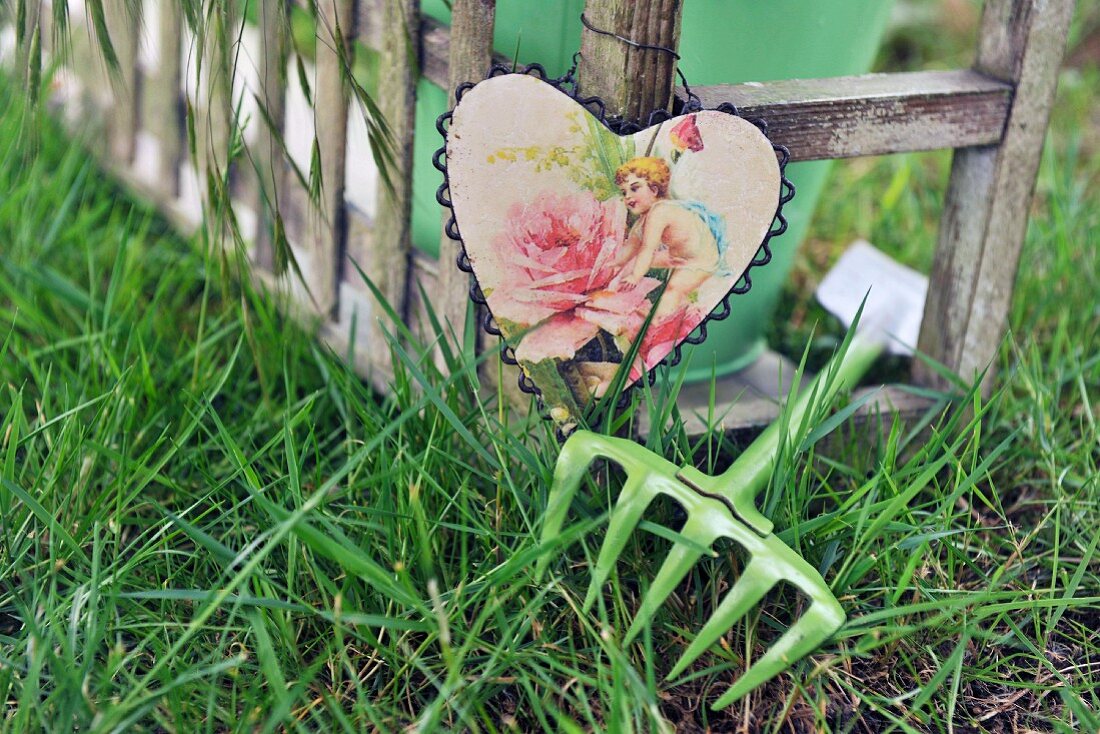 Heart-shaped picture hanging from frame of bench and gardening tool on lawn