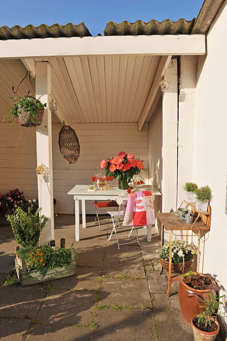 Table under white, wood-panelled loggia and planters on sunny terrace