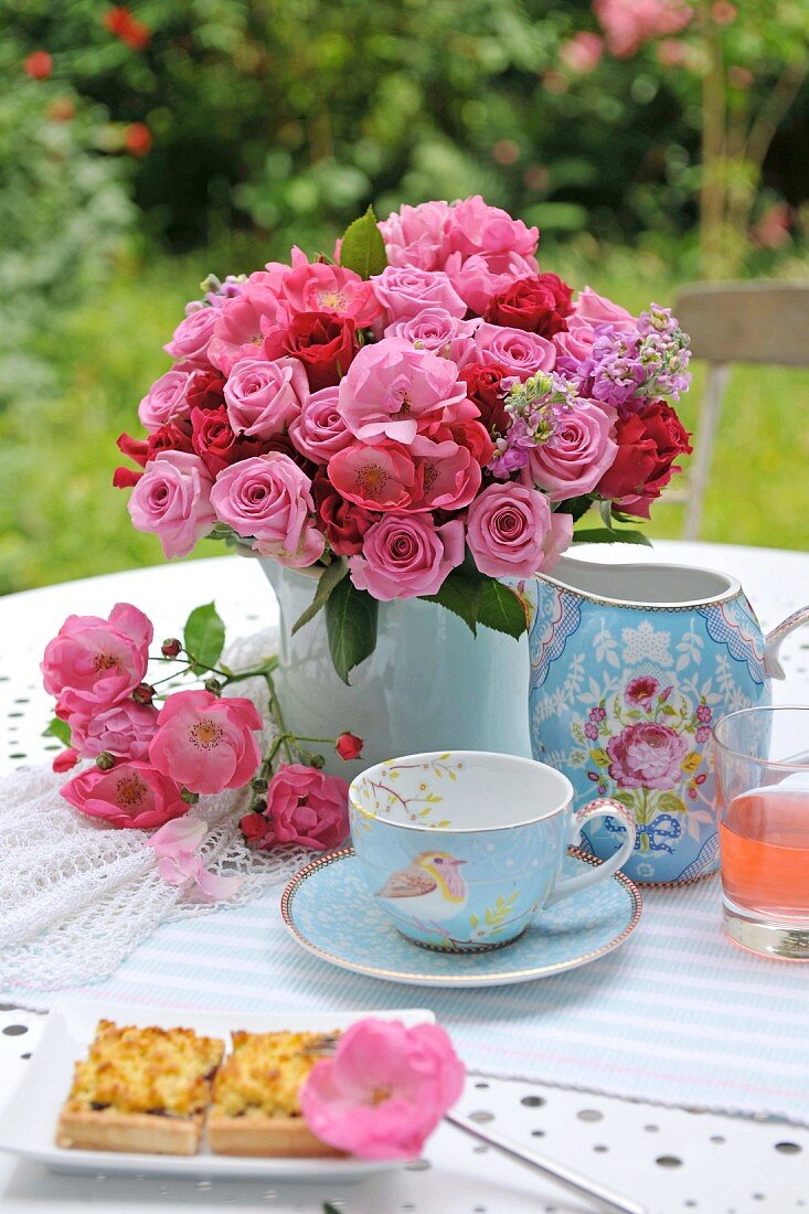 Tea and cake in garden with bouquet of roses in porcelain vase