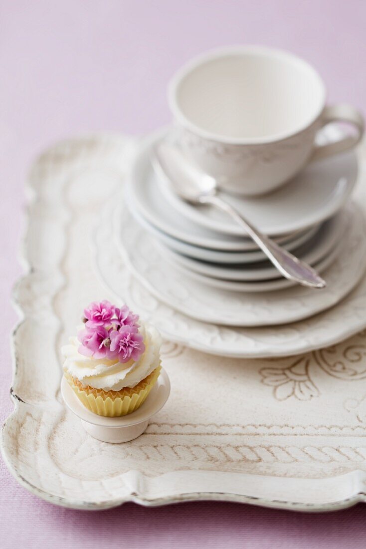 A cupcake on a tray with a stack of plates and a teacup