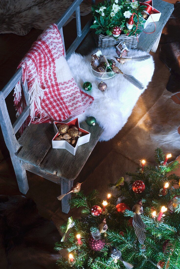 Christbaumdeko und weisses Fell auf rustikaler Bank neben geschmücktem Weihnachtsbaum