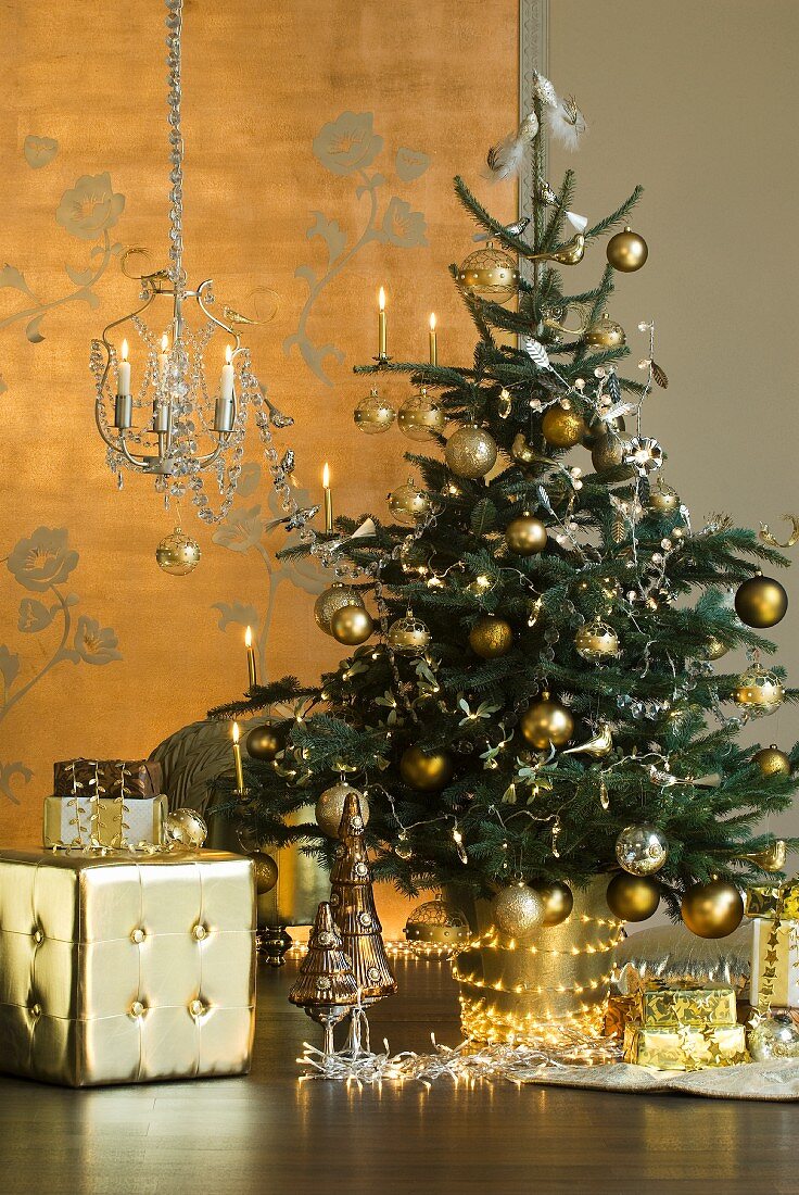 Gold geschmückter Weihnachtsbaum mit Lichterkette, davor goldfarbener Würfel-Hocker