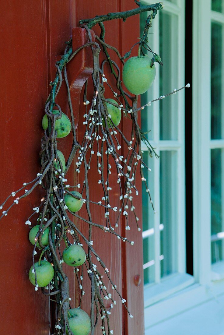 Zweig mit grünen Äpfeln umwickelt mit Leuchtzweigen als Türdeko