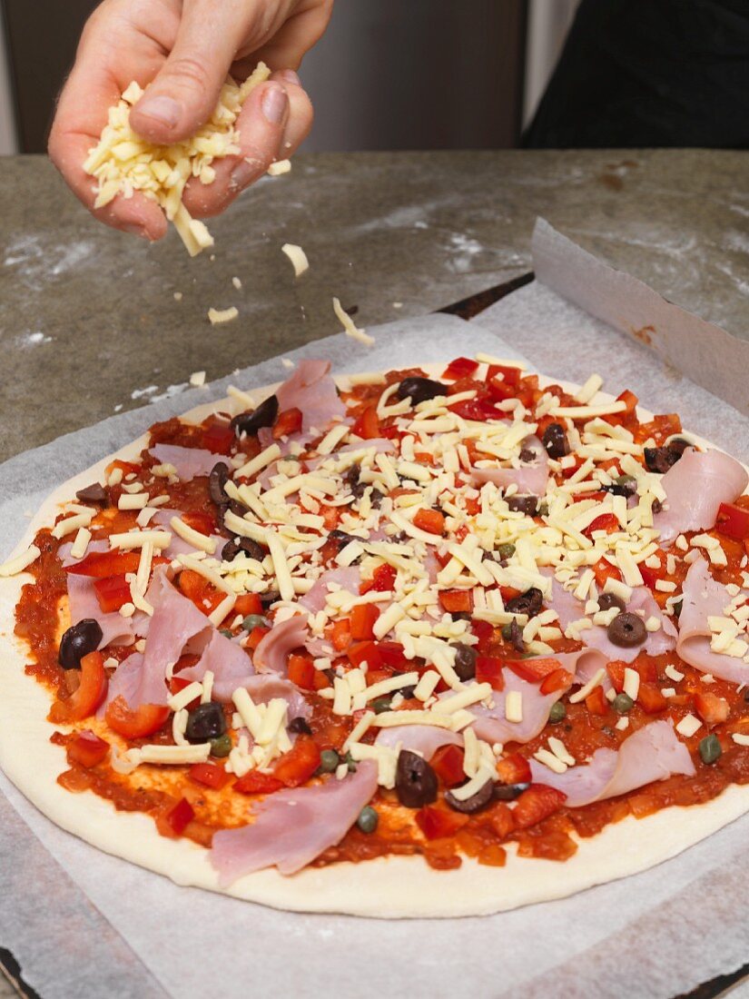 Pizza wird mit geriebenem Käse bestreut