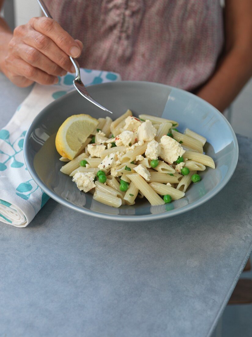 A woman eating penne pasta with feta cheese, peas and lemons