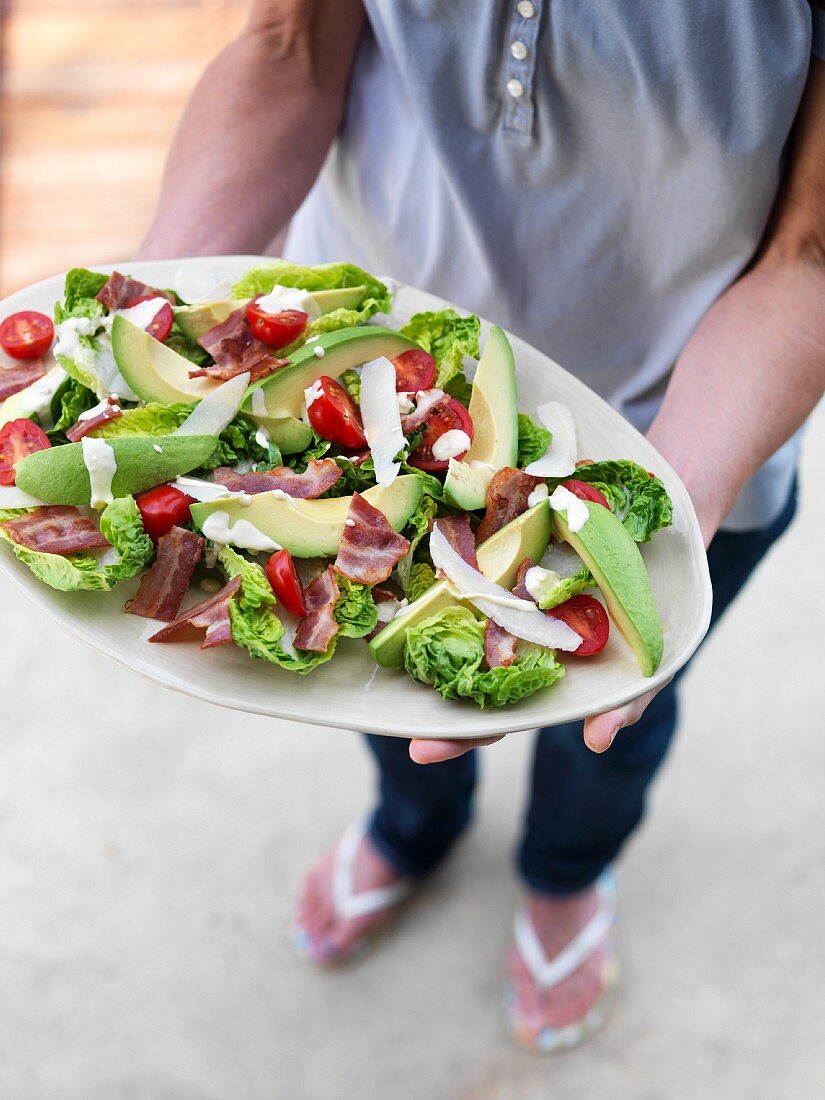 A woman holding a serving platter of avocado salad