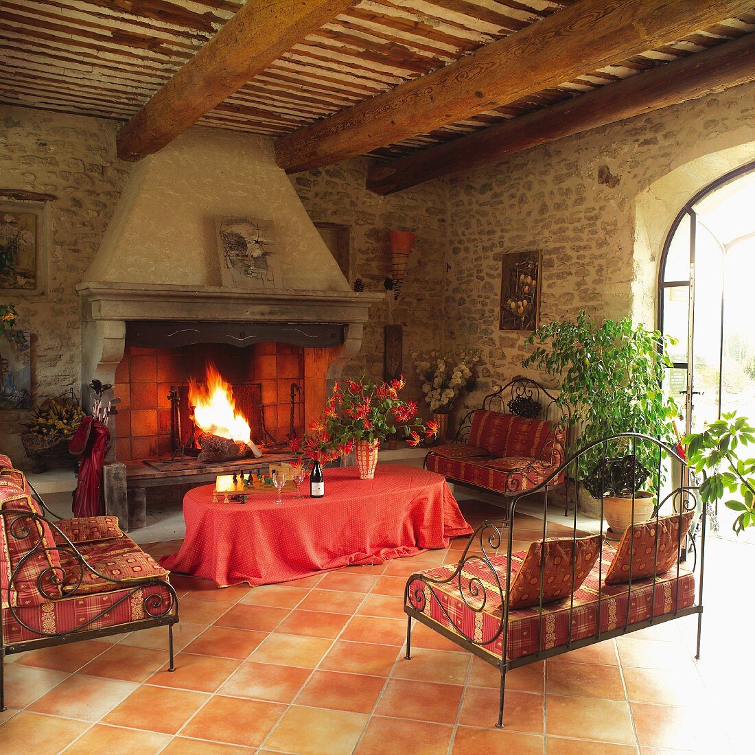 Inviting seating area with Provençal-patterned cushions on delicate metal sofas in front of imposing stone fireplace