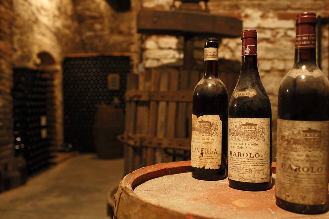 Dusty bottles on barrel in wine cellar with stone walls