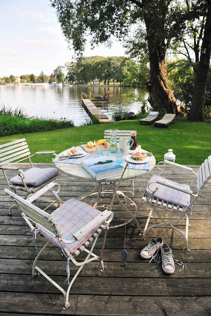 Essplatz auf der Terrasse - weiße Stühle und Tisch auf Holzdeck mit Blick auf den Weiher