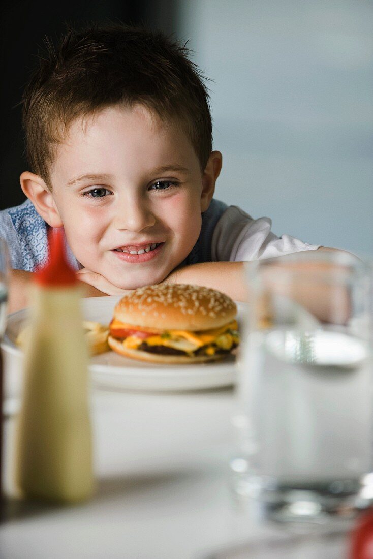 A little boy sitting at a table with a cheeseburger