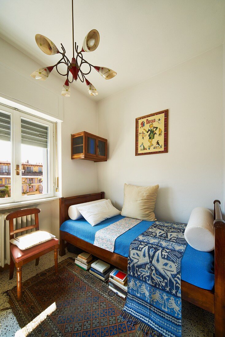 Solid wooden 30s bed with blue covers and chair with leather seat as a bedside table below lamp with fifties-style cone-shaped lampshades