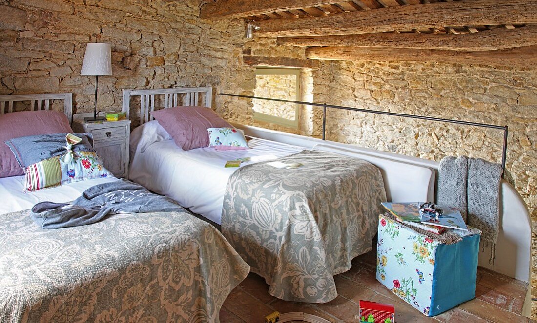 Twin beds on comfortable sleeping gallery with low wood-beamed ceiling and pale stone wall