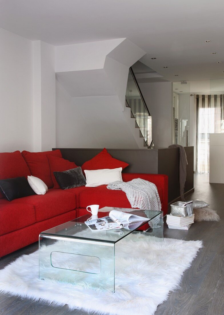Acrylic glass coffee table in front of red upholstered sofa in open-plan designer apartment with staircase