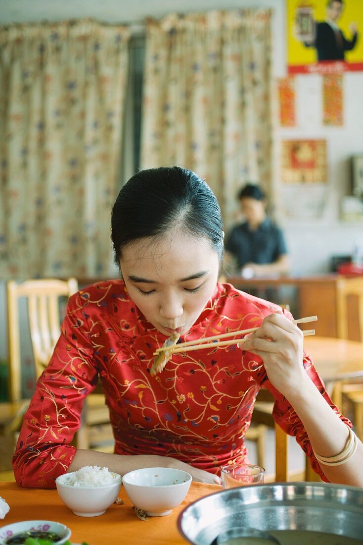 Young woman wearing traditional Chinese clothing, eating with chopsticks