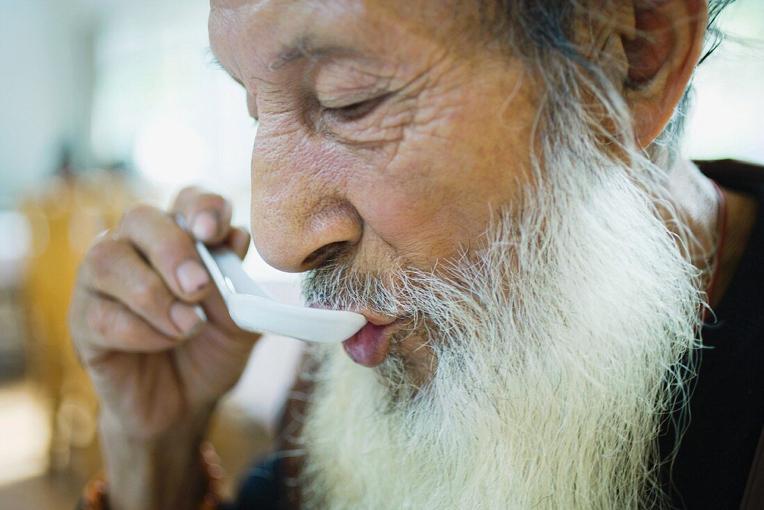 Elderly man with long beard eating with Chinese soup spoon