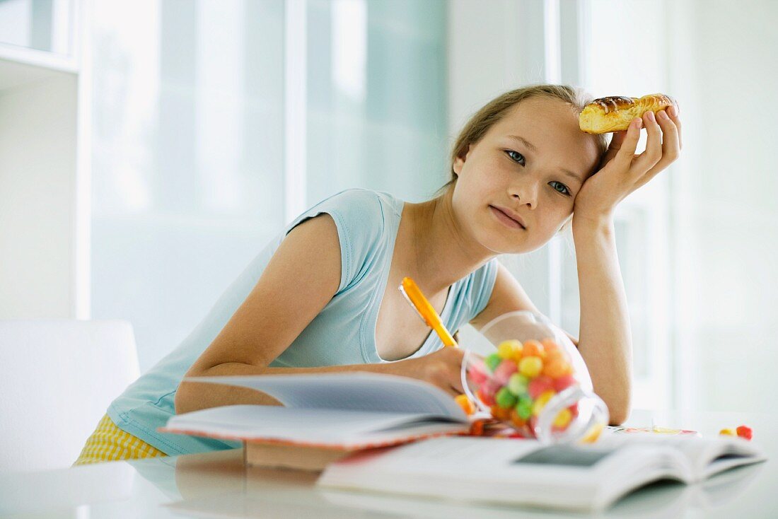 Mädchen isst Süssigkeiten bei den Hausaufgaben