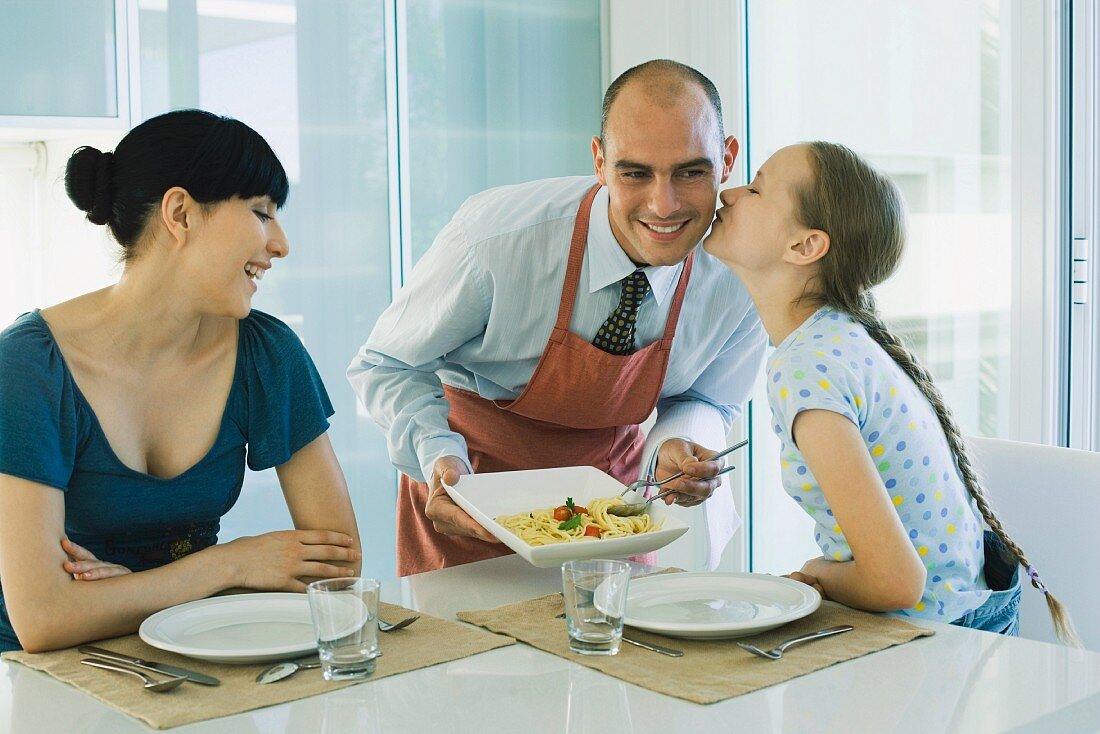 Man serving wife and daughter spaghetti, girl kissing father on cheek
