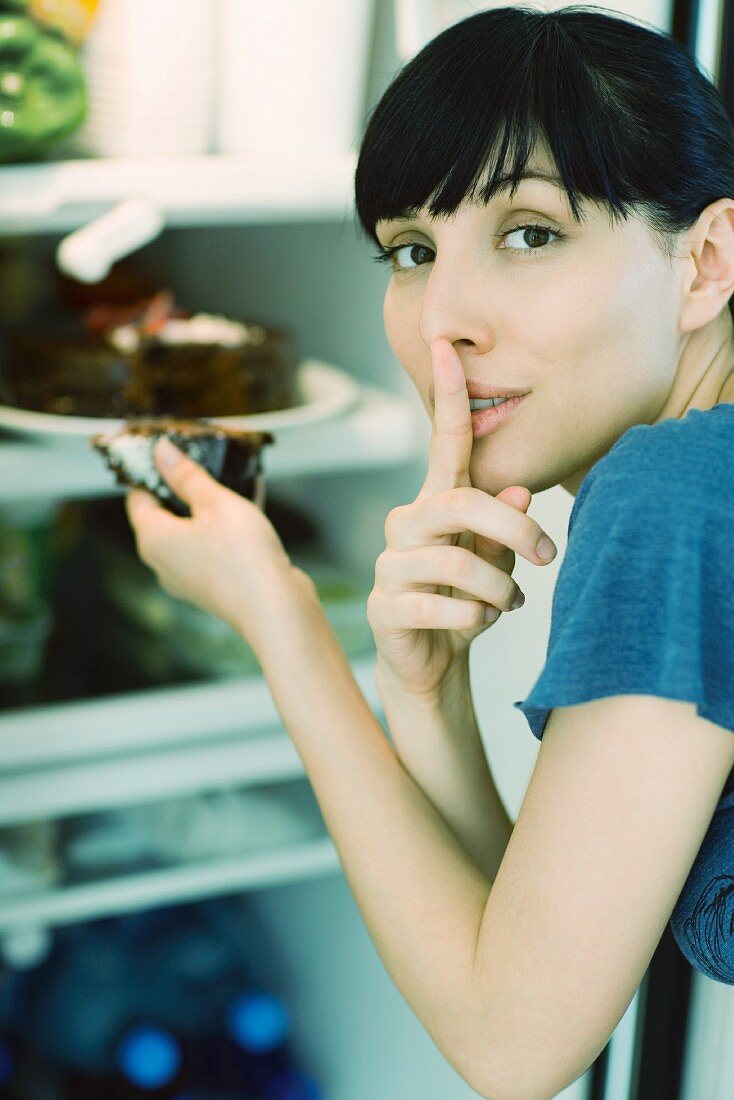 Frau nimmt ein Stück Kuchen aus dem Kühlschrank