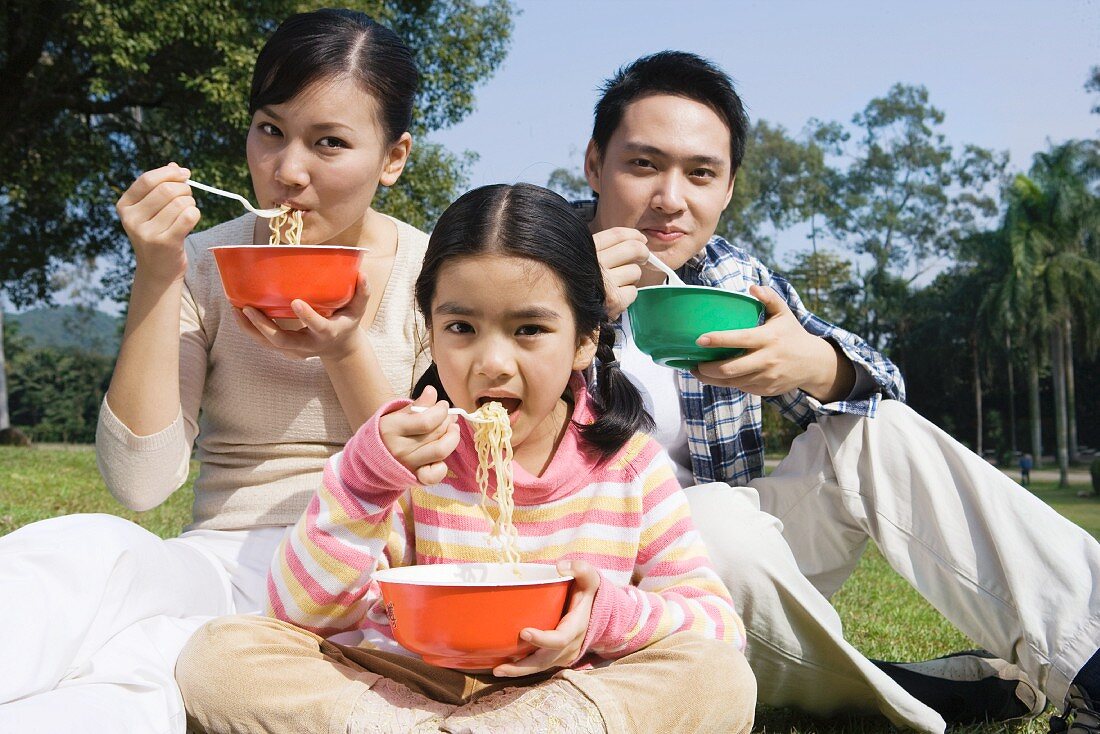 Asiatische Familie isst Nudelgericht im Park