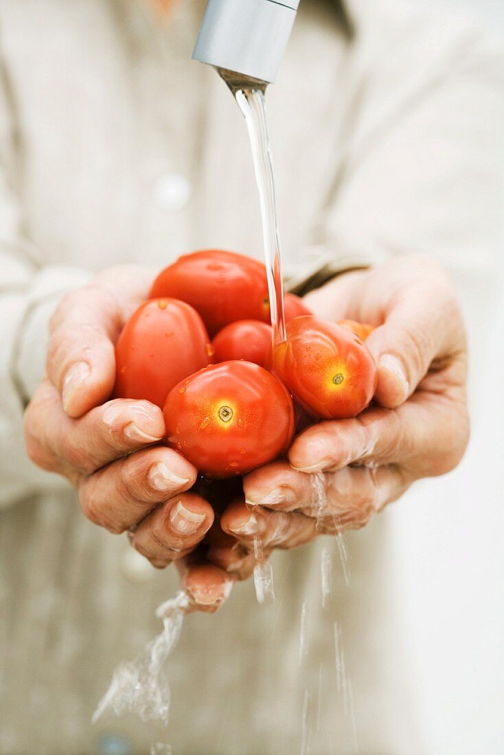 Woman rinsing handful of tomatoes under faucet, cropped view of hands