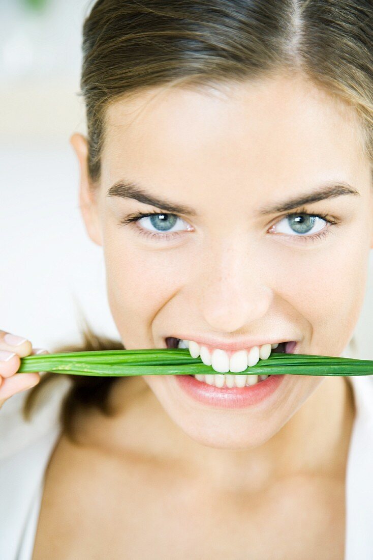 Woman holding chives between teeth, smiling at the camera, portrait