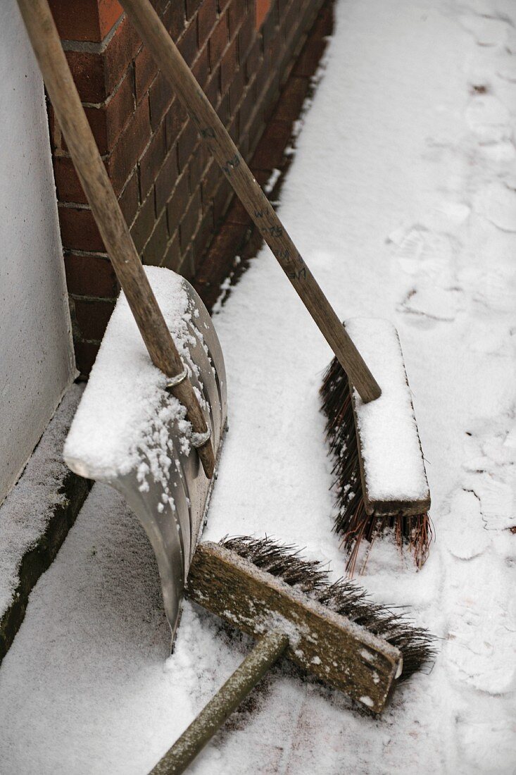 Two brooms and snow shovel at house wall